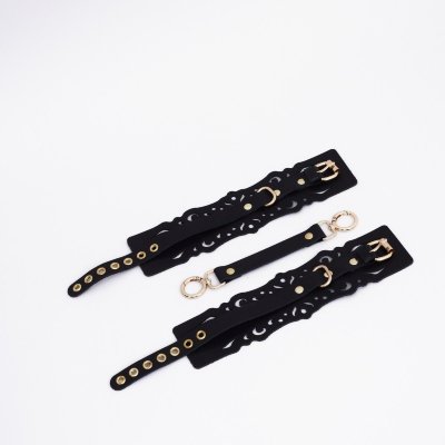 Черный кожаные оковы с узорами и золотистой фурнитурой Оковы с узорным дизайном из натуральной кожи с золотой фурнитурой. Резные элементы придают атмосферу нежности, элегантности и подчеркивают красоту тела. Регулируются ремешком, а также в комплекте прочный соединитель с двумя карабинами. Доставляется в фирменной упаковке в виде брендированной деревянной подложки. Длина манжеты - 25,5 см. Ширина манжеты - 7 см. Обхват - 24-33 см. Страна: Россия. Материал: натуральная кожа.